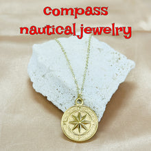 Load image into Gallery viewer, Gold compass necklace on a textured white stone with 'compass nautical jewelry' text.