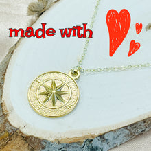 Load image into Gallery viewer, Gold compass pendant necklace on a white stone surface with red hearts and text.