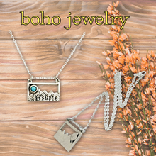 Load image into Gallery viewer, Boho jewelry necklace with mountain design on a wooden surface with flowers