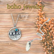 Load image into Gallery viewer, Boho jewelry with nature-themed pendant on a wooden surface with flowers.