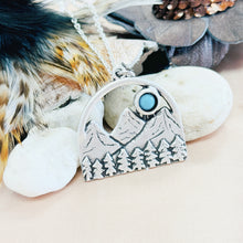 Load image into Gallery viewer, Silver mountain pendant with blue gemstone on a natural background with feathers and stones