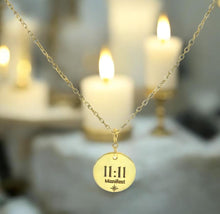 Load image into Gallery viewer, Gold necklace with a pendant displaying '11:11 Manifest' against a blurred candlelit background.