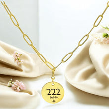 Load image into Gallery viewer, Gold necklace with a '222 Let Go' pendant on a soft fabric background