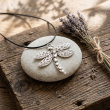 Load image into Gallery viewer, Artisan dragonfly necklace resting on smooth river stone and rustic wood table